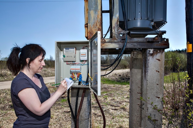 technician woman checking electricity meter invoice standing near electricity switchgear power transformer substation outdoors
