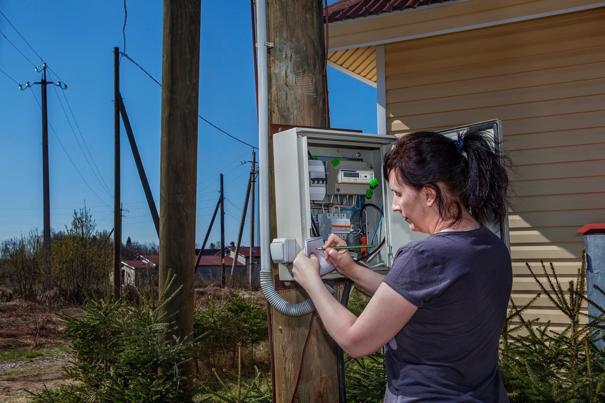 woman looking electric meter data switchgear mounted wooden pole near farm house countryside